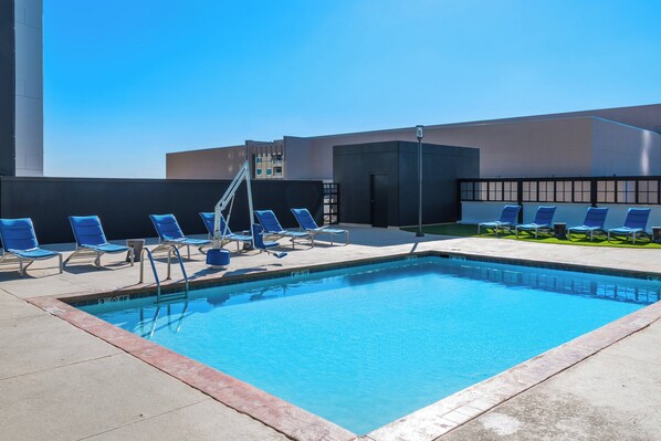 A rooftop pool with blue lounge chairs and a clear blue sky.