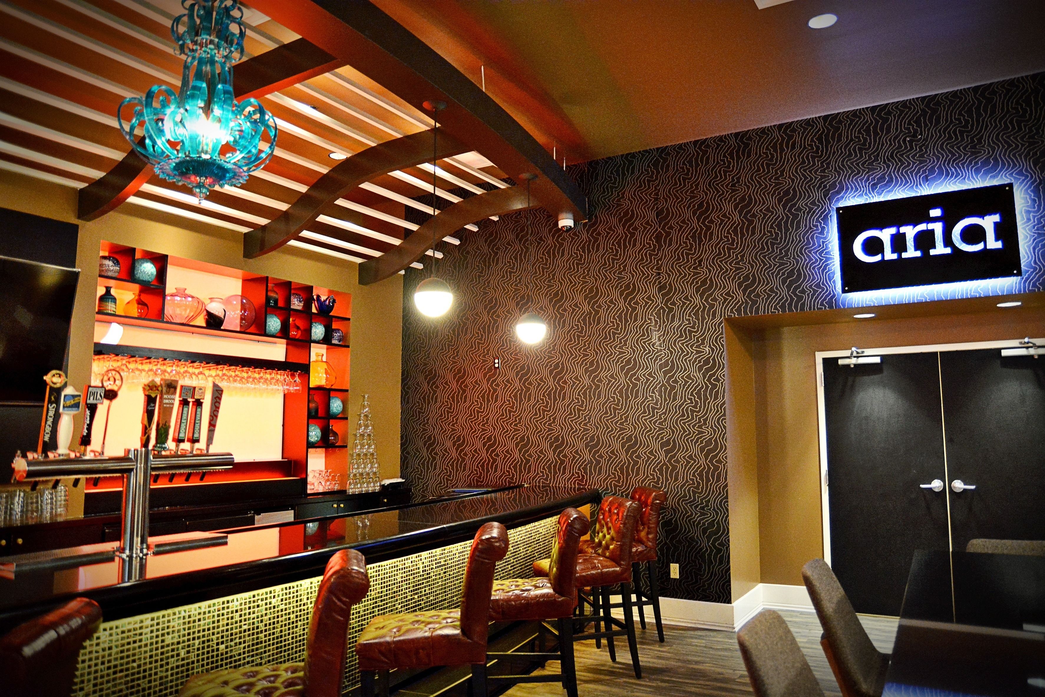 A bar area with a counter, bar stools, and a neon sign reading "aria".