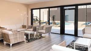 Una sala de estar moderna con sofá, sillones y una mesa de centro. Se ve una piscina a través de amplias puertas de vidrio.