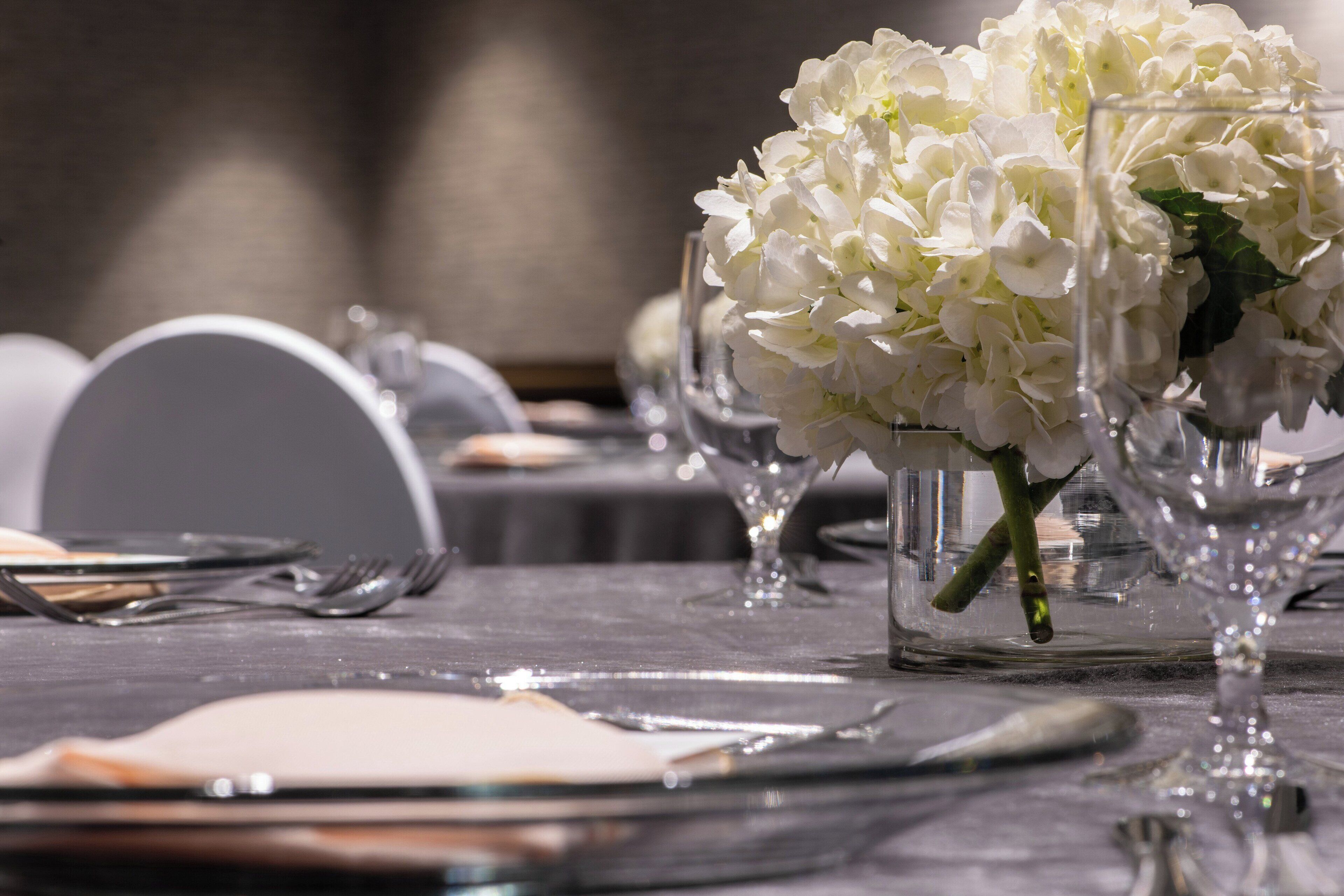A table set with white flowers in glass vases, silverware, and plates.