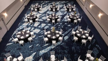 Un amplio salón banqueteado con alfombra, con varias mesas redondas y sillas blancas, dispuestas en un patrón simétrico.