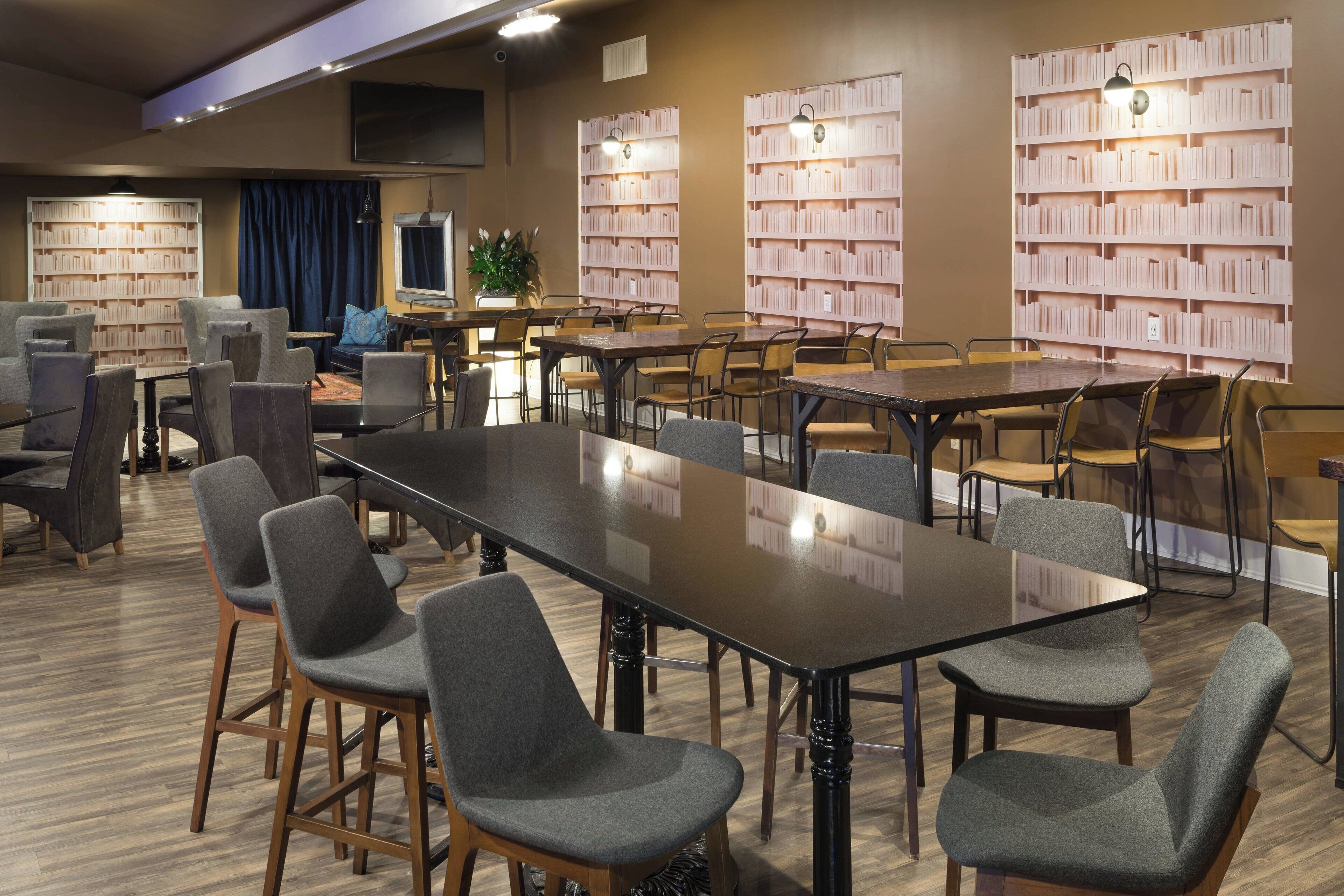 A modern library with multiple tables and chairs, bookshelves, and a television.