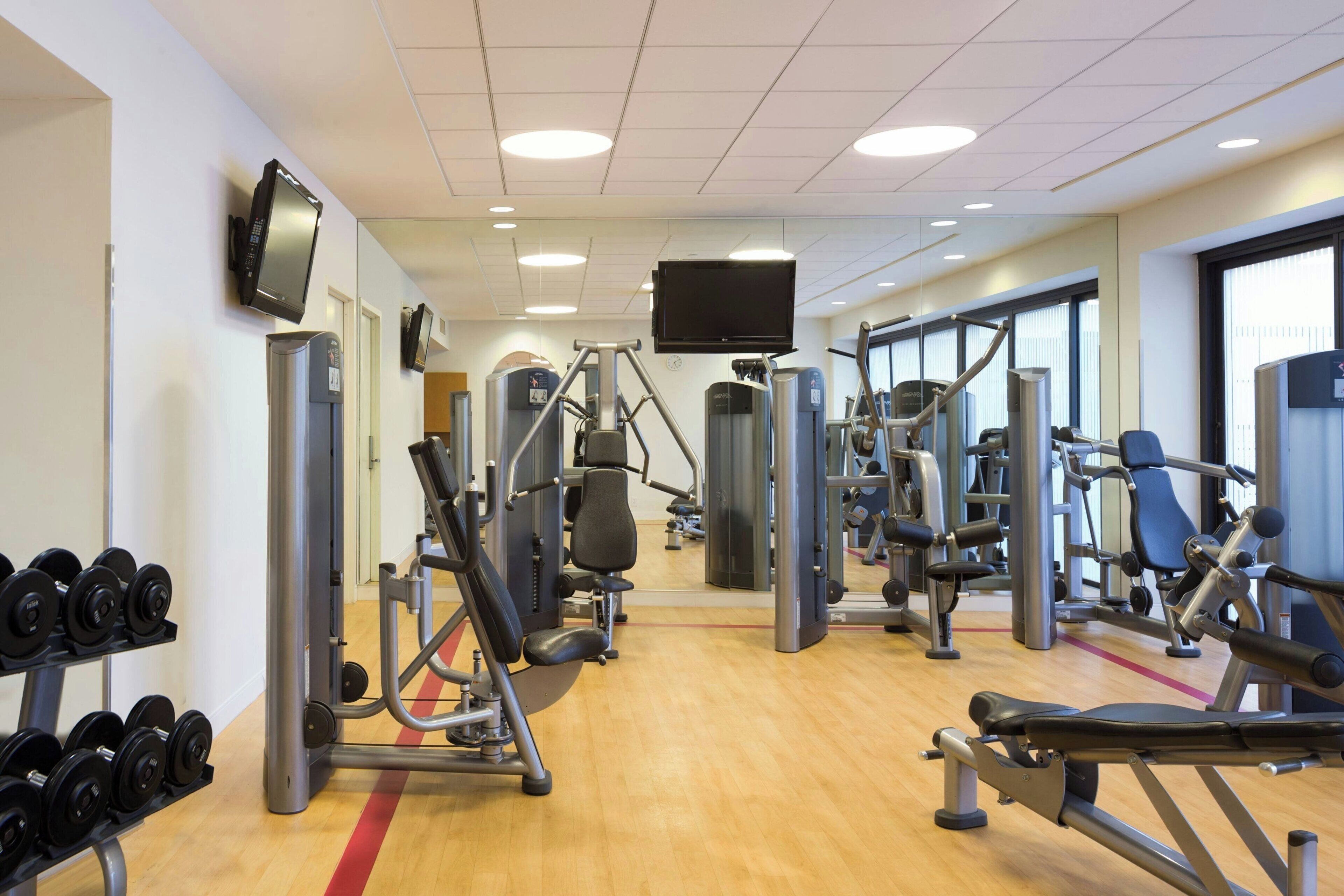 Une salle de sport équipée de divers appareils d’entraînement, de poids libres et d’un écran de télévision fixé au mur.