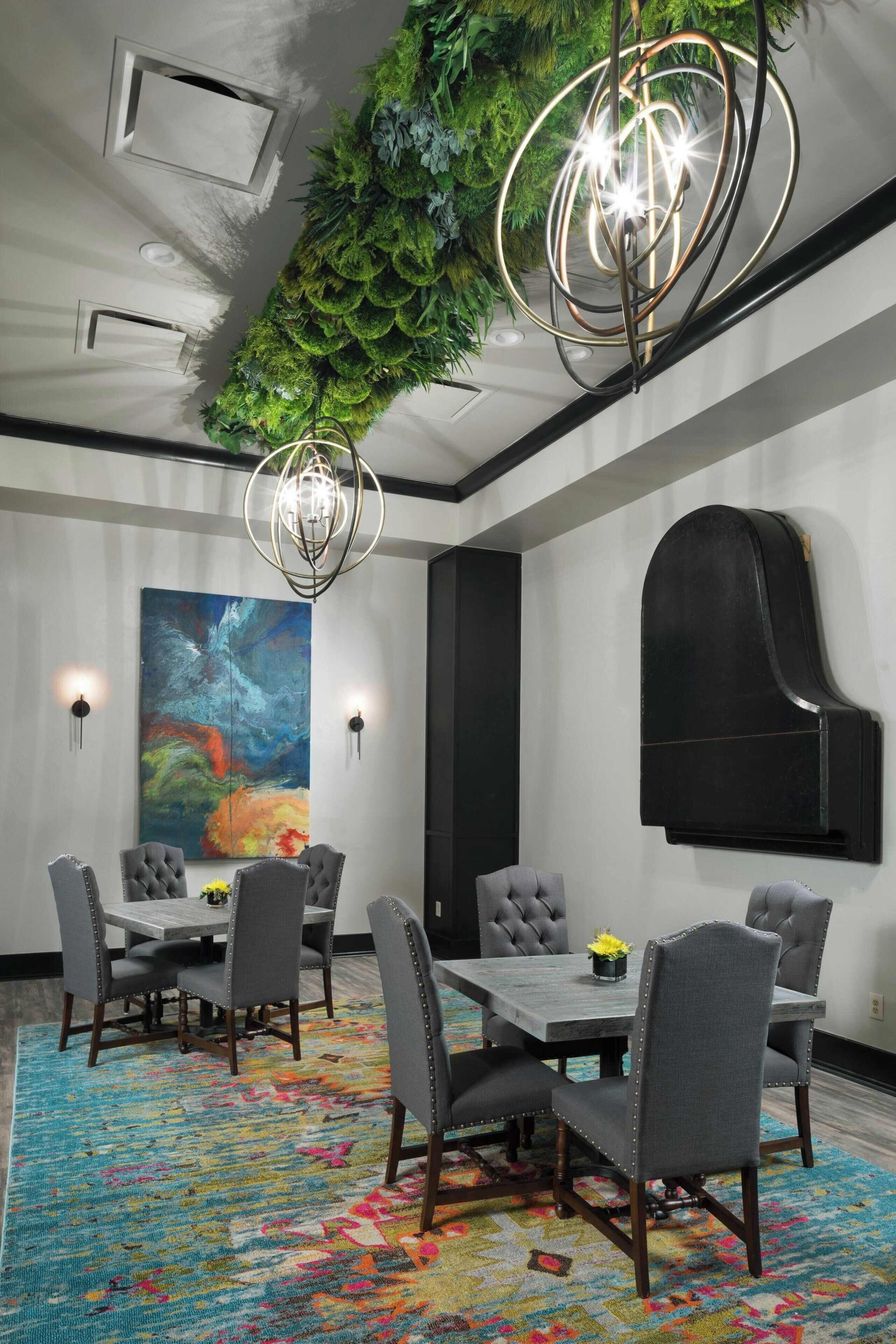A modern conference room with a large table, grey upholstered chairs, a colorful rug, a green wall hanging, and a large abstract painting.