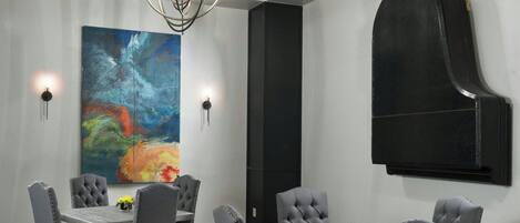 A modern conference room with a large table, grey upholstered chairs, a colorful rug, a green wall hanging, and a large abstract painting.