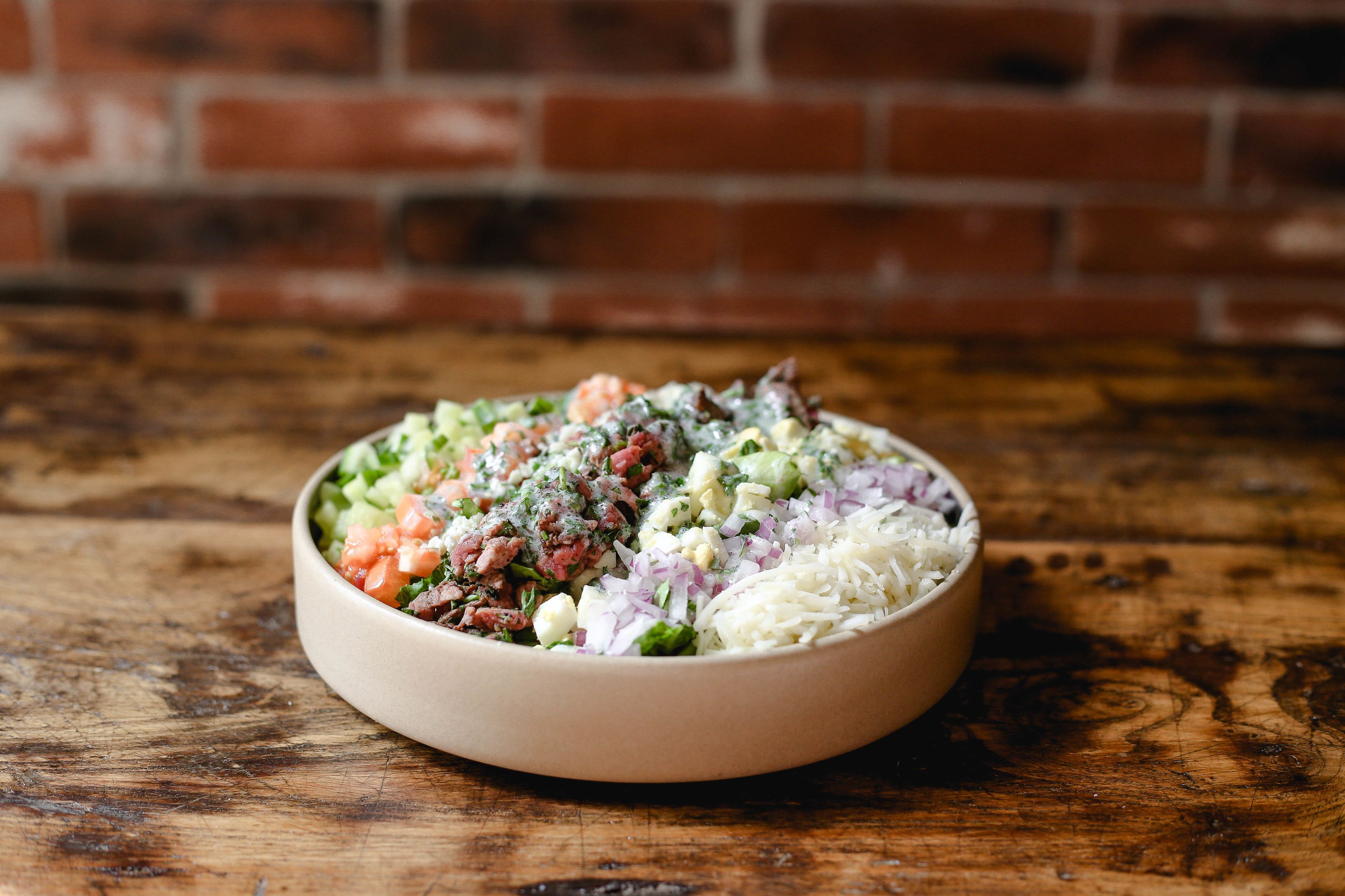 A bowl of salad on a wooden table with a brick wall in the background.