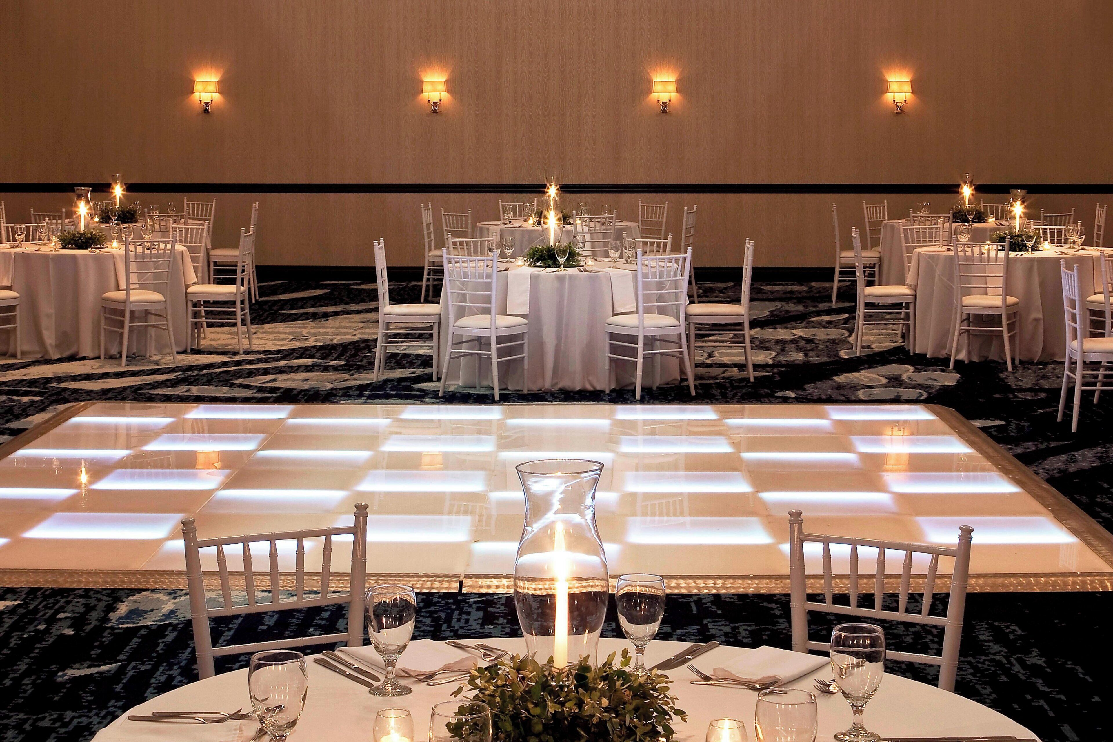 A banquet hall with round tables, white chairs, and a checkered dance floor.