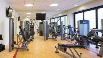 A gym with various exercise machines, a television, and large windows.