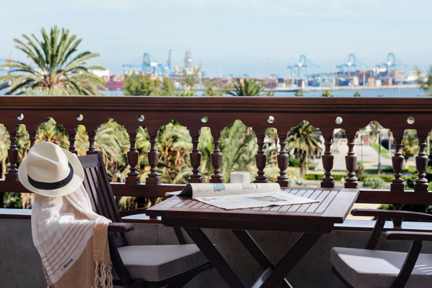 A wooden balcony with a view of a port and palm trees.