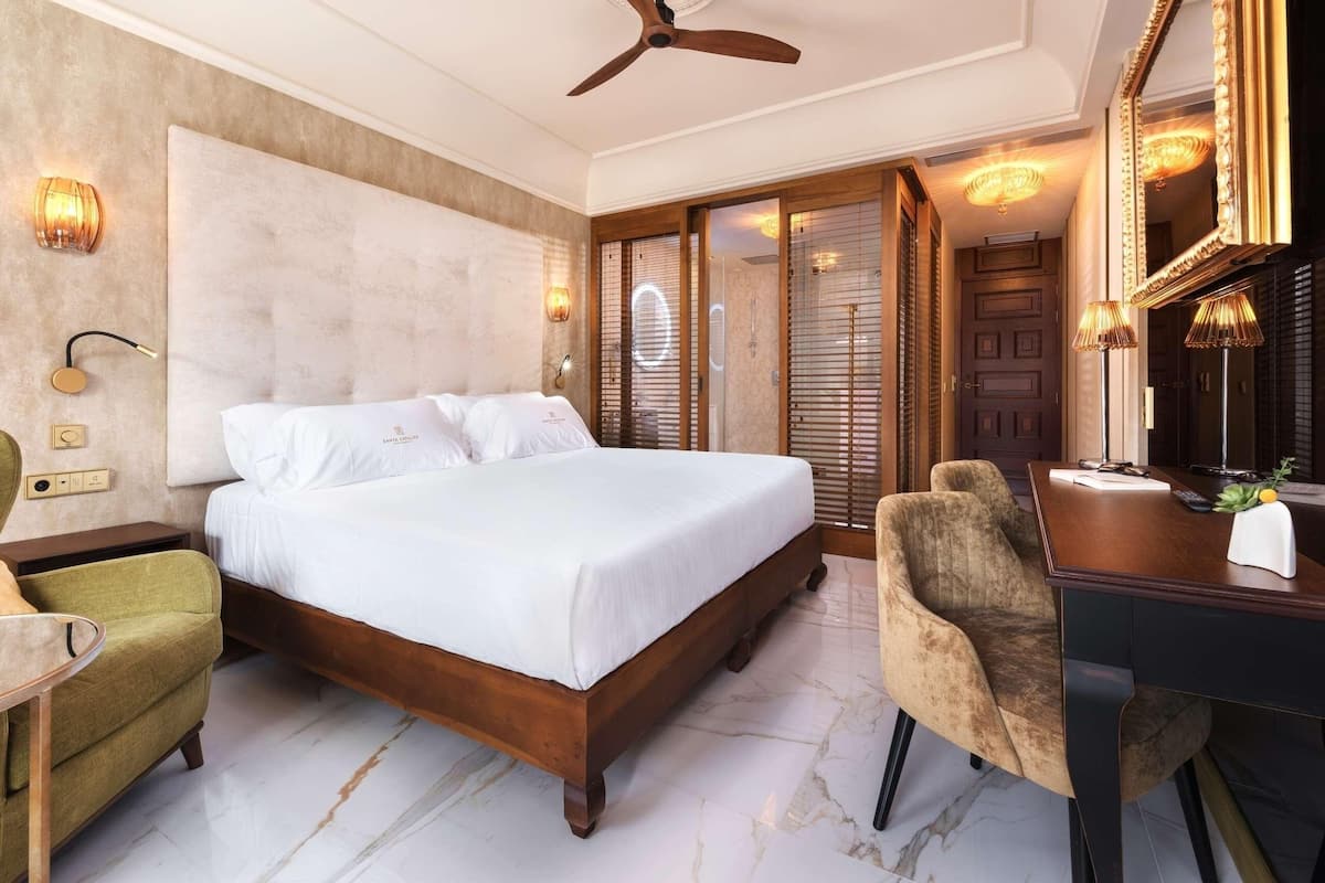 Un dormitorio con una cama grande, un escritorio, una silla, un ventilador de techo y un espejo.