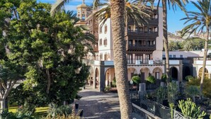Ein Innenhof mit Palmen, ein Gebäude mit Bögen und eine Kuppel im Hintergrund.
