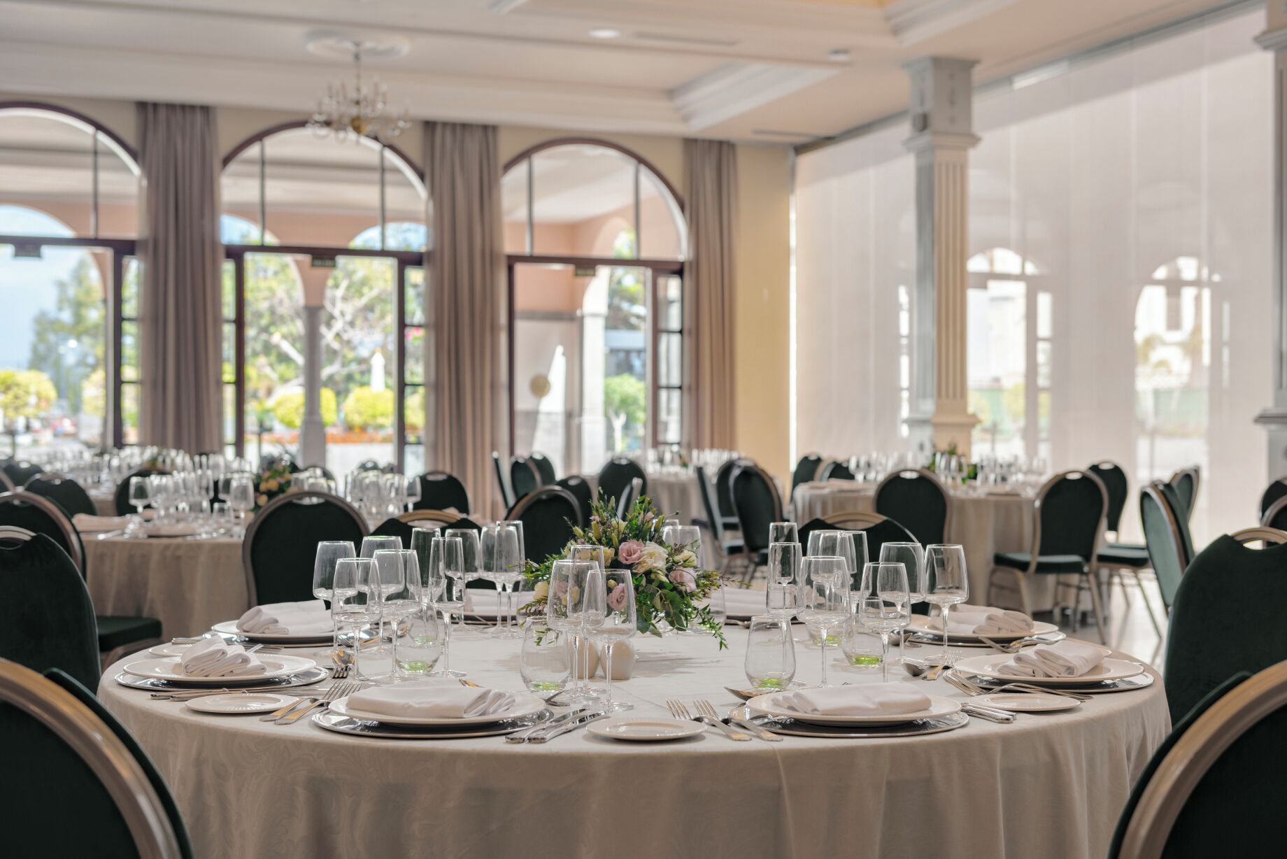Une salle de banquet avec des tables rondes dressées pour un événement formel, agrémentée de nappes blanches, de verres et de compositions florales.