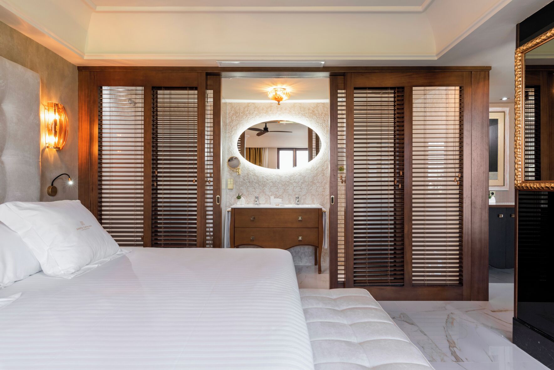 A bedroom with a large bed, a vanity with a mirror, and wooden sliding doors.