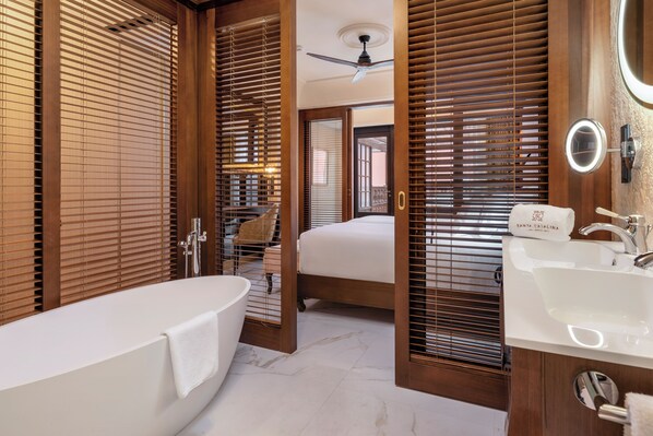 Un baño moderno con bañera, lavamanos y persianas de madera.