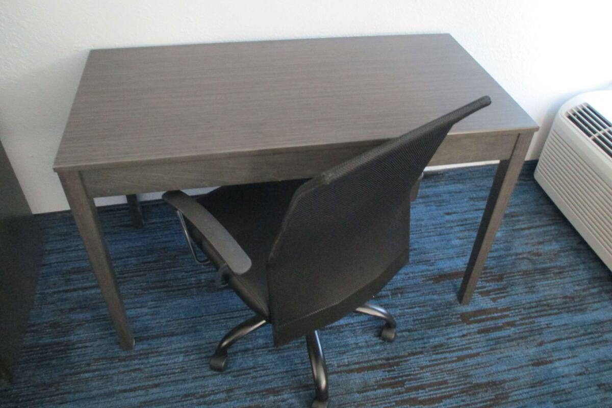 Een kleine kantoorruimte met een bureau, stoel, vloerbedekking en een wandradiator.