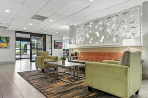 Un hall d’entrée comprenant un canapé, des fauteuils, une table basse, un tapis à motifs et un mur décoratif.