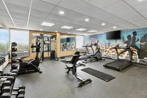 Un gimnasio con cintas de correr, elípticas, pesas sueltas y un espejo grande.