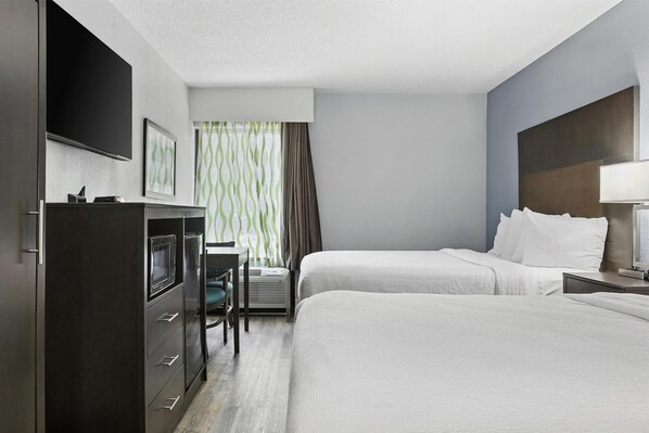 A hotel room with two beds, a desk, a TV, and a window with curtains.
