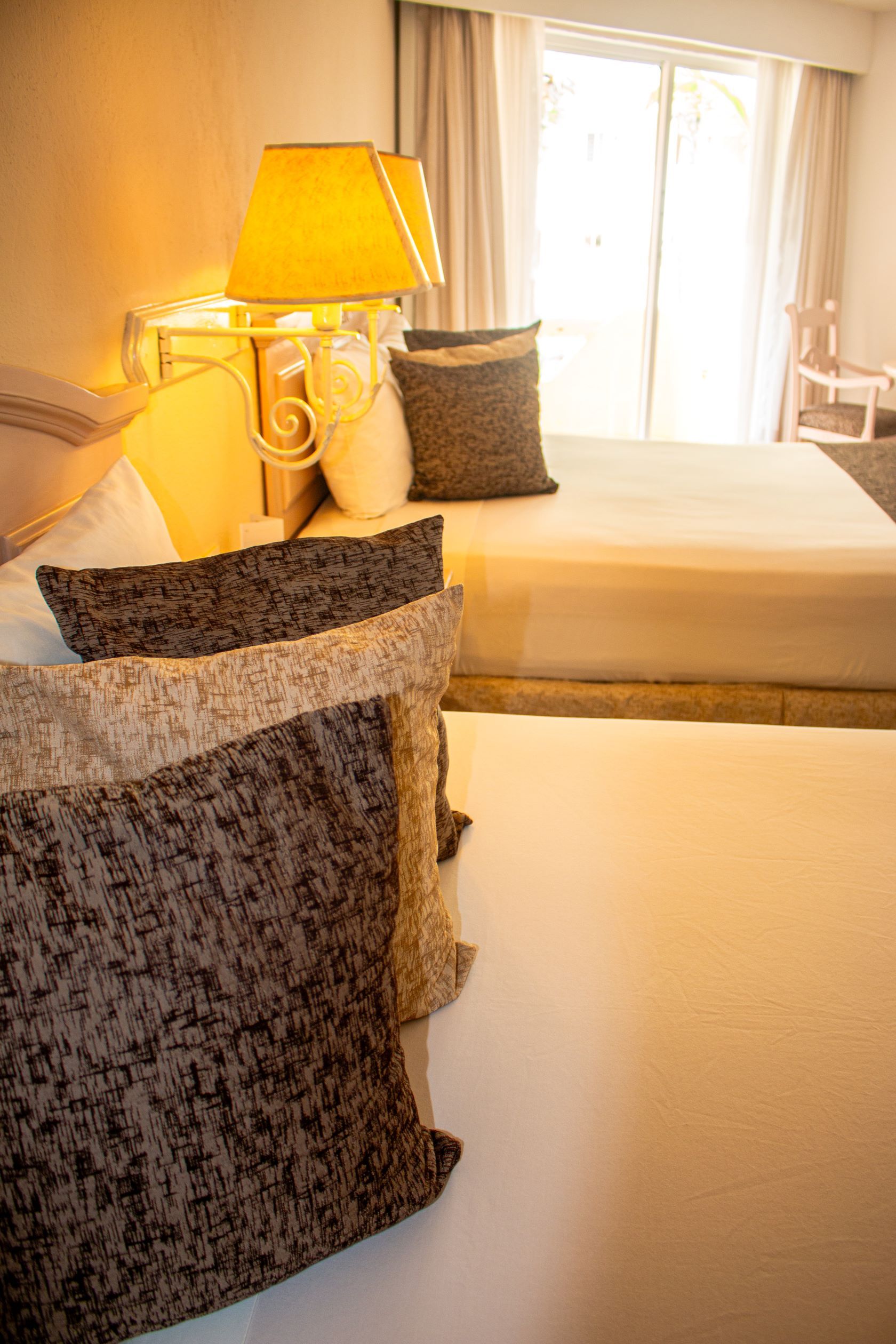 A hotel room with two beds, a lamp, and a window with curtains.