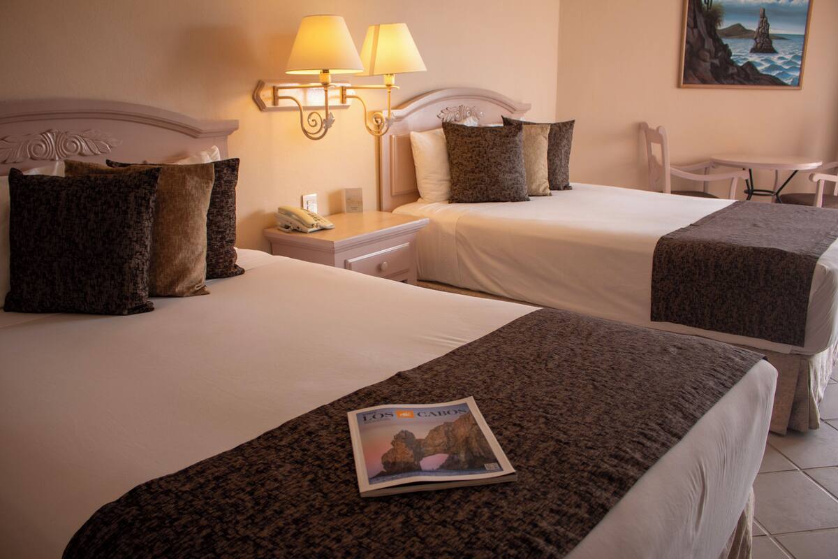 Two beds with headboards, a nightstand, a lamp, a magazine on the bed, and a chair.