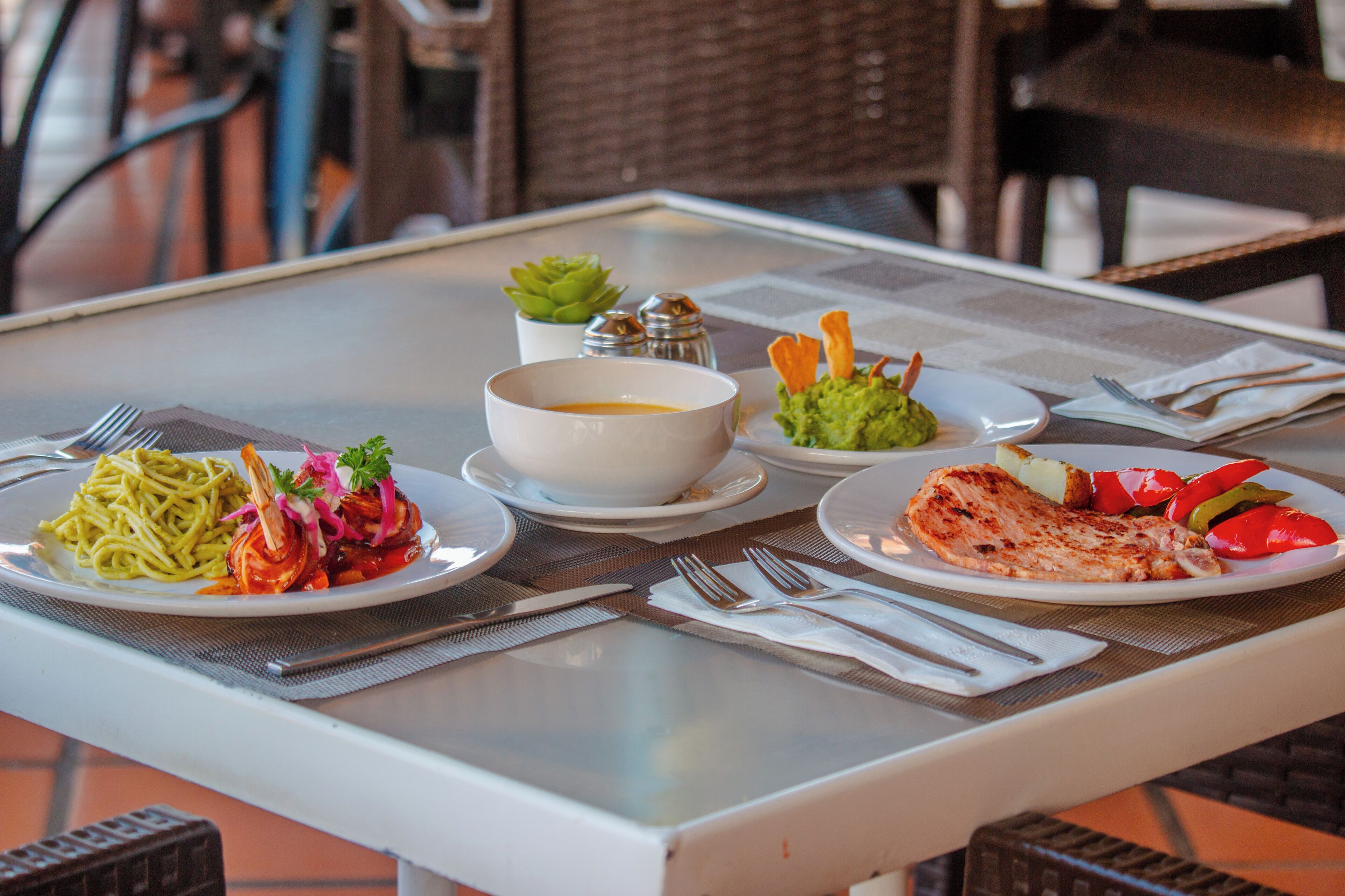 A table set with plates of pasta, a bowl of soup, a plate of grilled chicken, and vegetables.