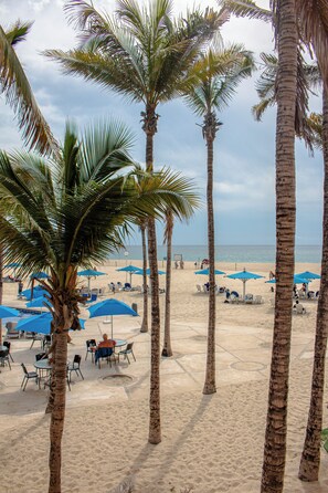 A beach with palm trees, blue umbrellas, and beach chairs. - Posada Real Los Cabos (San José del Cabo)