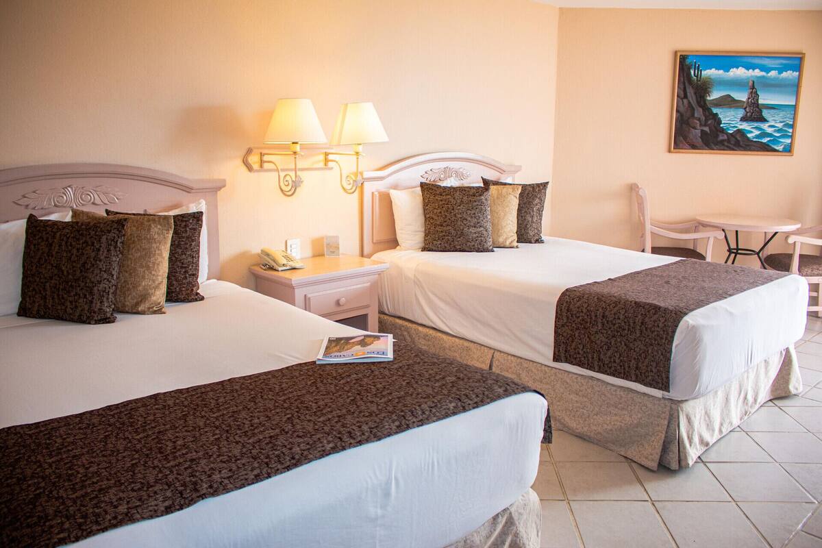 A hotel room with two beds, a nightstand, a table, and a chair.