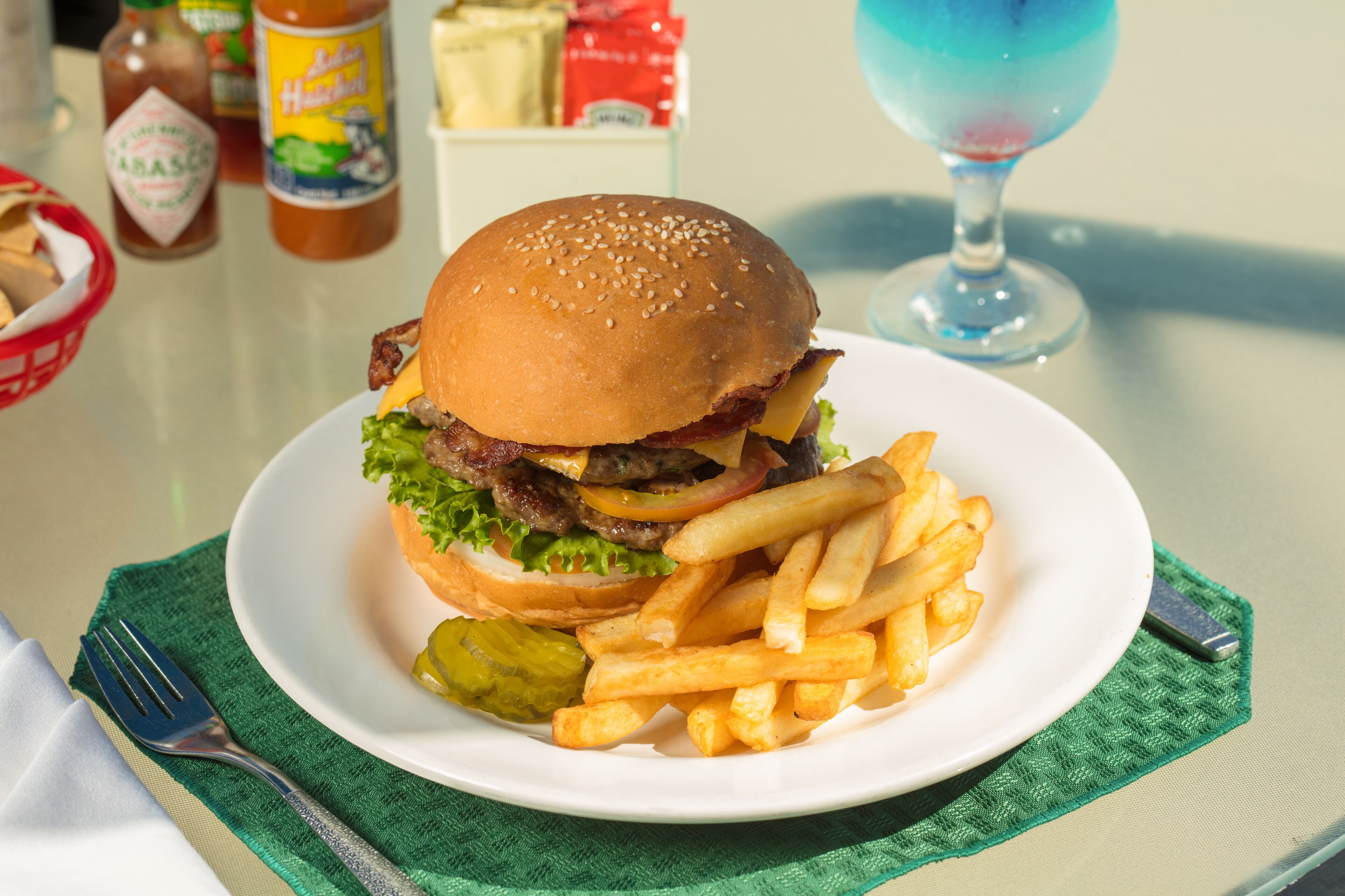 A plate with a hamburger and fries, a pickle, and condiments on a table.