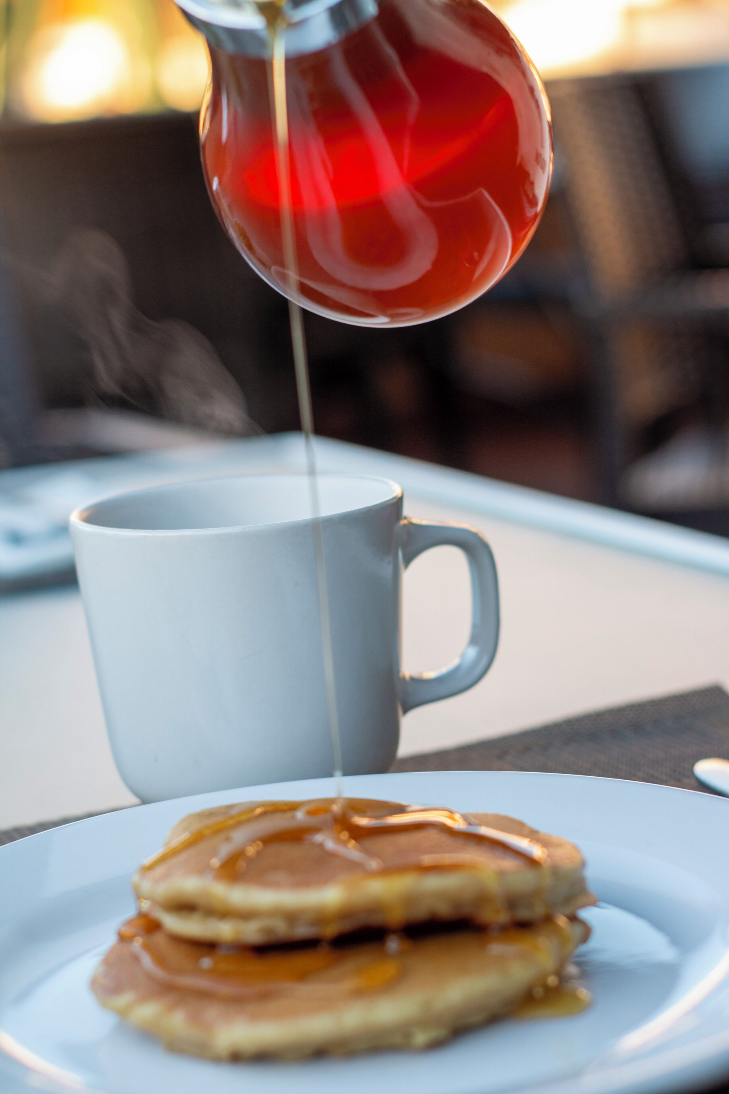 Eine weiße Tasse und ein Teller mit Pfannkuchen und Sirup.