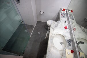 Un baño con cabina de ducha de vidrio, inodoro y lavamanos de mármol con espejo.