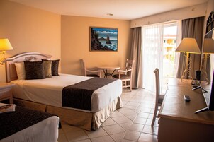 Habitación de hotel con cama, escritorio, silla, lámpara y un cuadro en la pared.