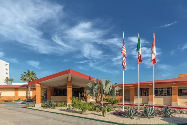 A hotel with a red roof, palm trees, and three flags.