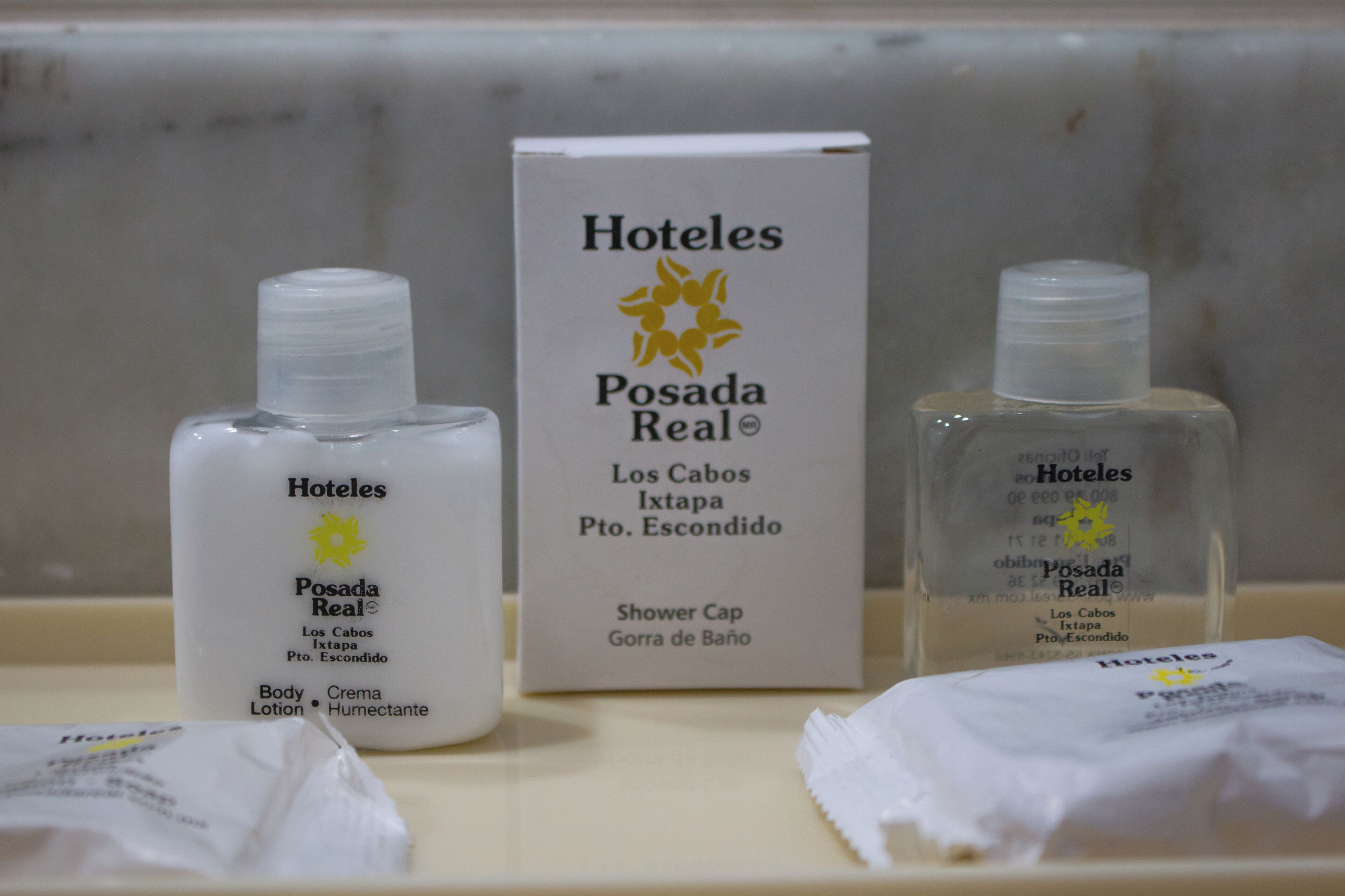 Baño de hotel con artículos de aseo, incluyendo loción corporal, gorro de ducha y una caja de productos de la marca del hotel.