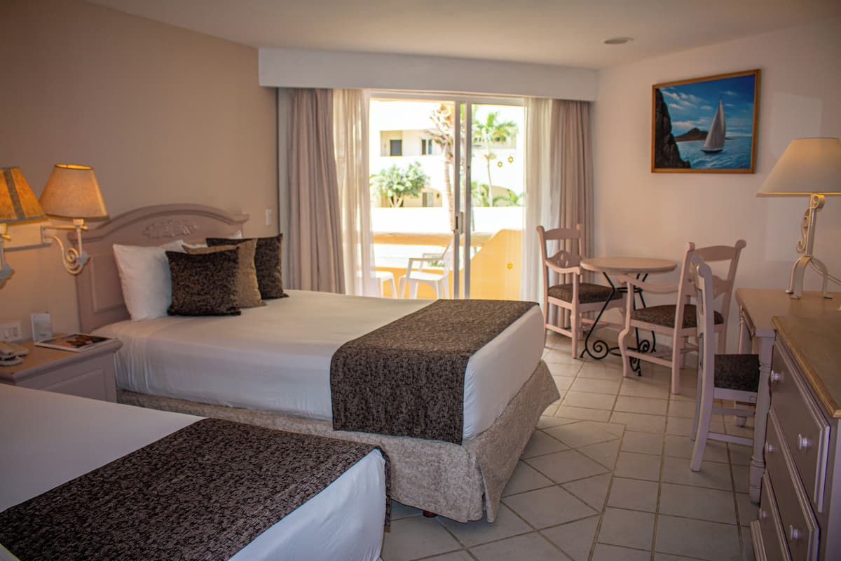 A hotel room with two beds, a desk, a chair, and a view of the outdoors.