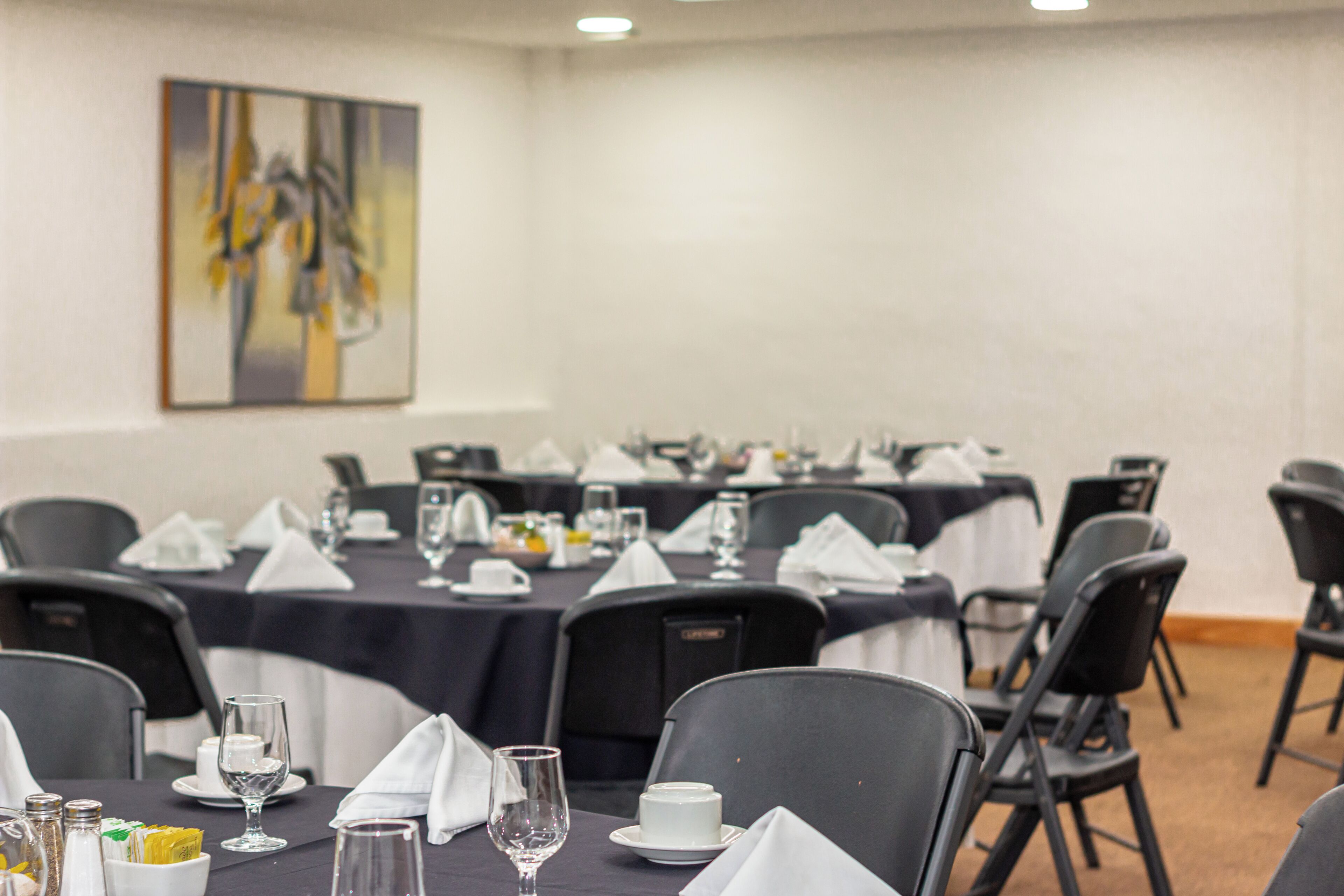 A conference room with tables set for a meeting, chairs arranged around them, and a painting on the wall.