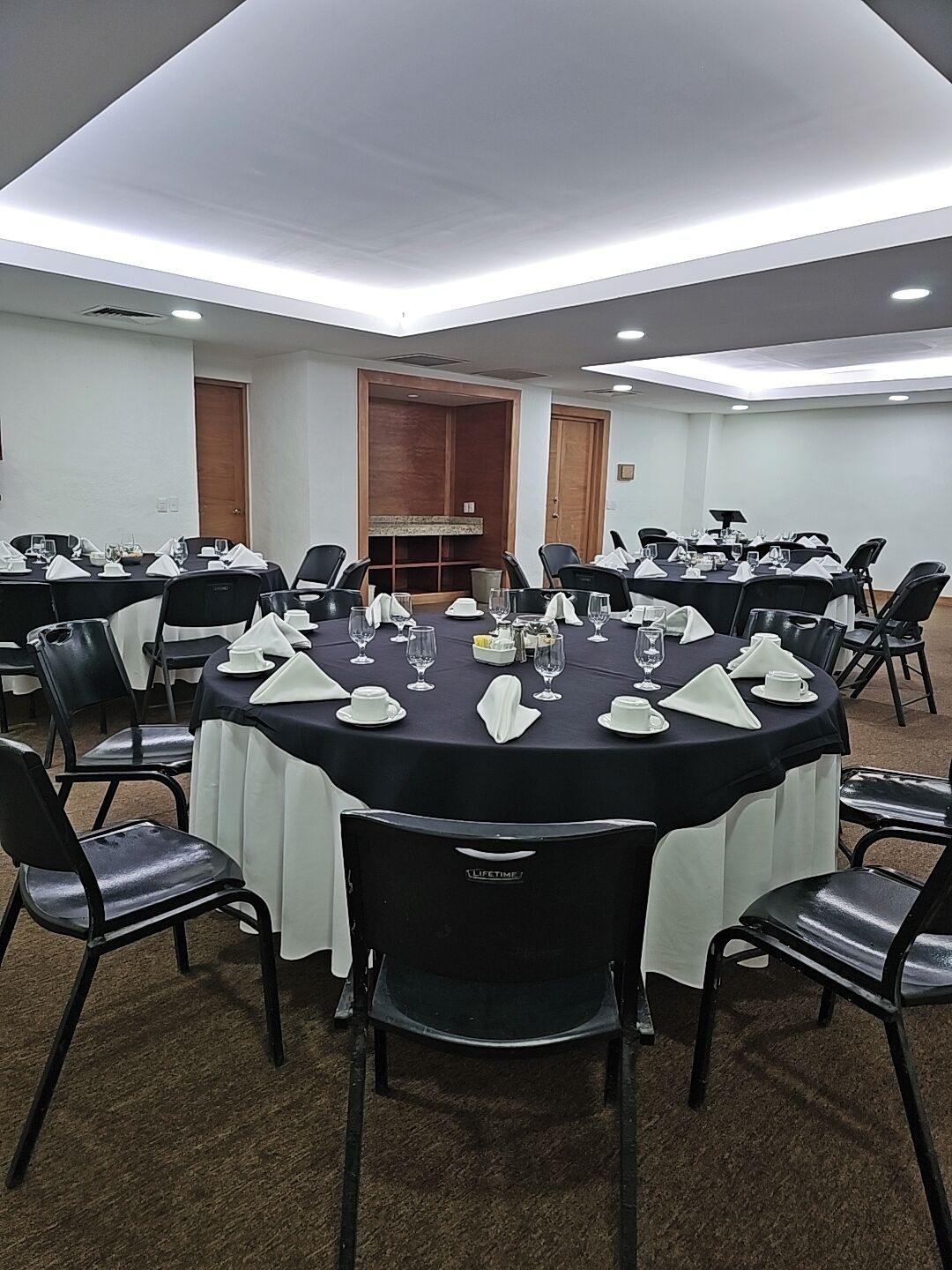 Un salón de conferencias con mesas redondas, sillas negras y manteles blancos.