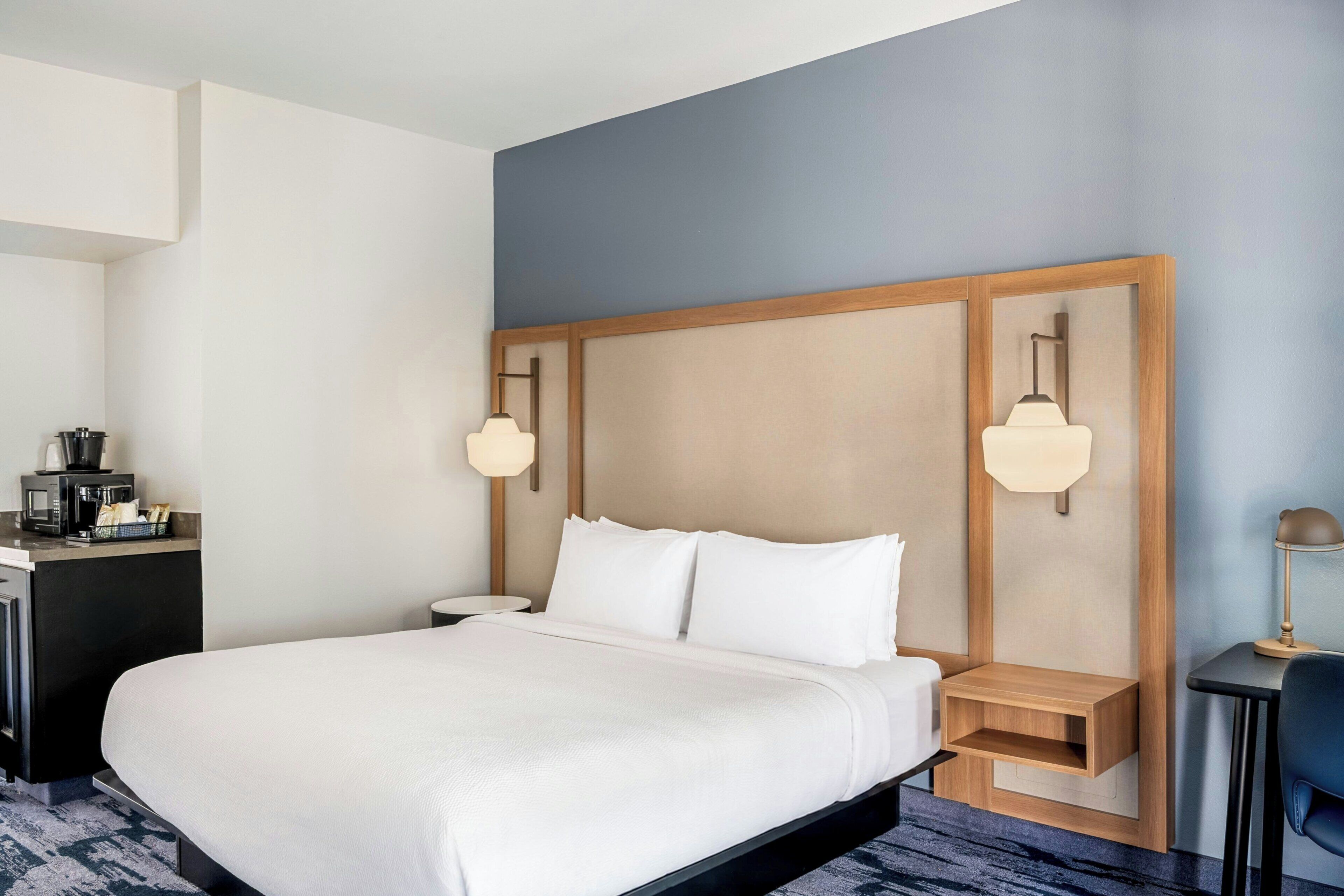 A hotel room with a large bed, bedside tables, a desk with a coffee maker, and a lamp.