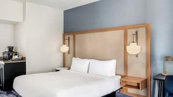 Una habitación de hotel con una cama grande, mesitas de noche, un escritorio con cafetera y una lámpara.