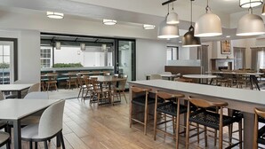Un moderno comedor con varias mesas y sillas, iluminación colgante y vistas al exterior.