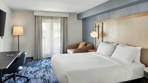Habitación de hotel con cama, escritorio, silla, televisor y ventana con cortinas.