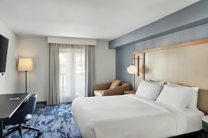 Habitación de hotel con cama, escritorio, silla, televisor y ventana con cortinas.