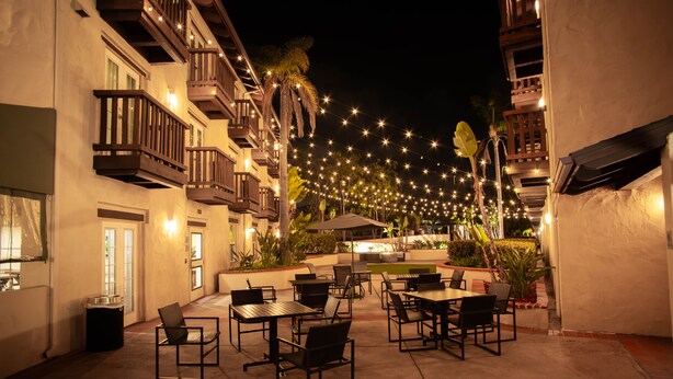 Un patio al aire libre con mesas, sillas, luces colgantes y un edificio con balcones.