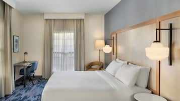 Une chambre d’hôtel avec un grand lit, un bureau avec une chaise, une lampe et une fenêtre avec des rideaux.