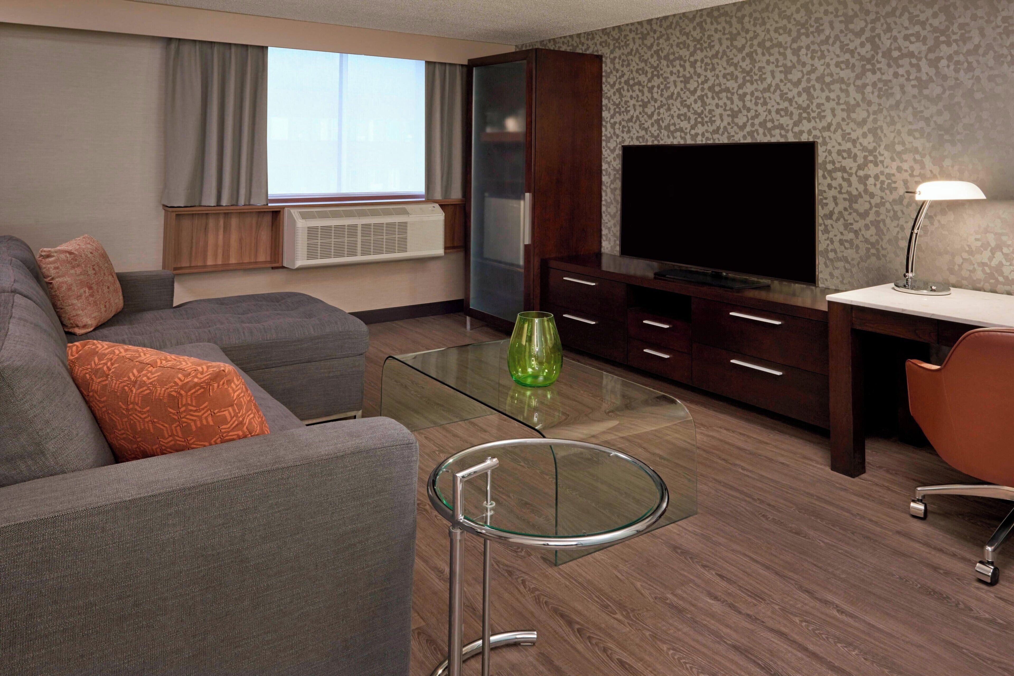 A modern living room with a sofa, a glass coffee table, a TV, and a desk with a lamp.