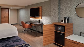 A hotel room with a bed, a desk with a chair, a coffee maker, and a wardrobe.