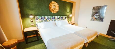 A hotel room with a large bed, a green headboard, a decorative mirror, a nightstand, a lamp, and a framed picture on the wall.