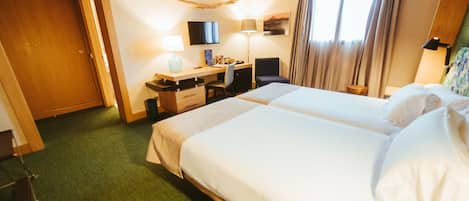 A hotel room with a large bed, a desk with a chair, a television, and a window with curtains.