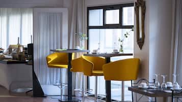 A modern dining area with a table set for four, surrounded by yellow chairs, a decorative mirror, and a window with curtains.