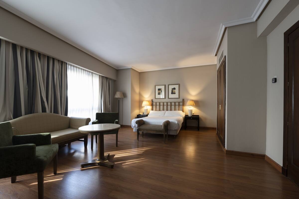 Una habitación de hotel con una cama, un sofá, una mesita y una lámpara.