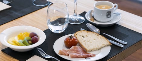 A breakfast setting with a plate of toast, smoked salmon, a bowl of fruit, a glass of orange juice, and a cup of coffee.